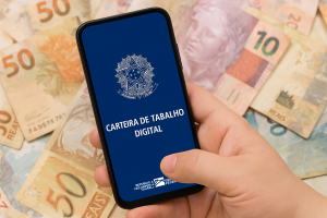 Pessoa segurando um smartphone que exibe a tela inicial do aplicativo "Carteira de Trabalho Digital", com várias cédulas de real brasileiro ao fundo, simbolizando a organização financeira e o acesso facilitado a benefícios como o Consignado do Trabalhador, que oferece crédito com condições diferenciadas para quem possui registro formal.