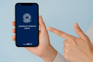 Pessoa segurando um smartphone que exibe a tela inicial do aplicativo "Carteira de Trabalho Digital", com o brasão da República Federativa do Brasil e fundo azul, destacando a praticidade do acesso ao documento trabalhista de forma eletrônica.