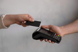 Cliente realizando pagamento por aproximação com cartão preto em uma máquina de cartão moderna, demonstrando a praticidade da tecnologia contactless no comércio atual.