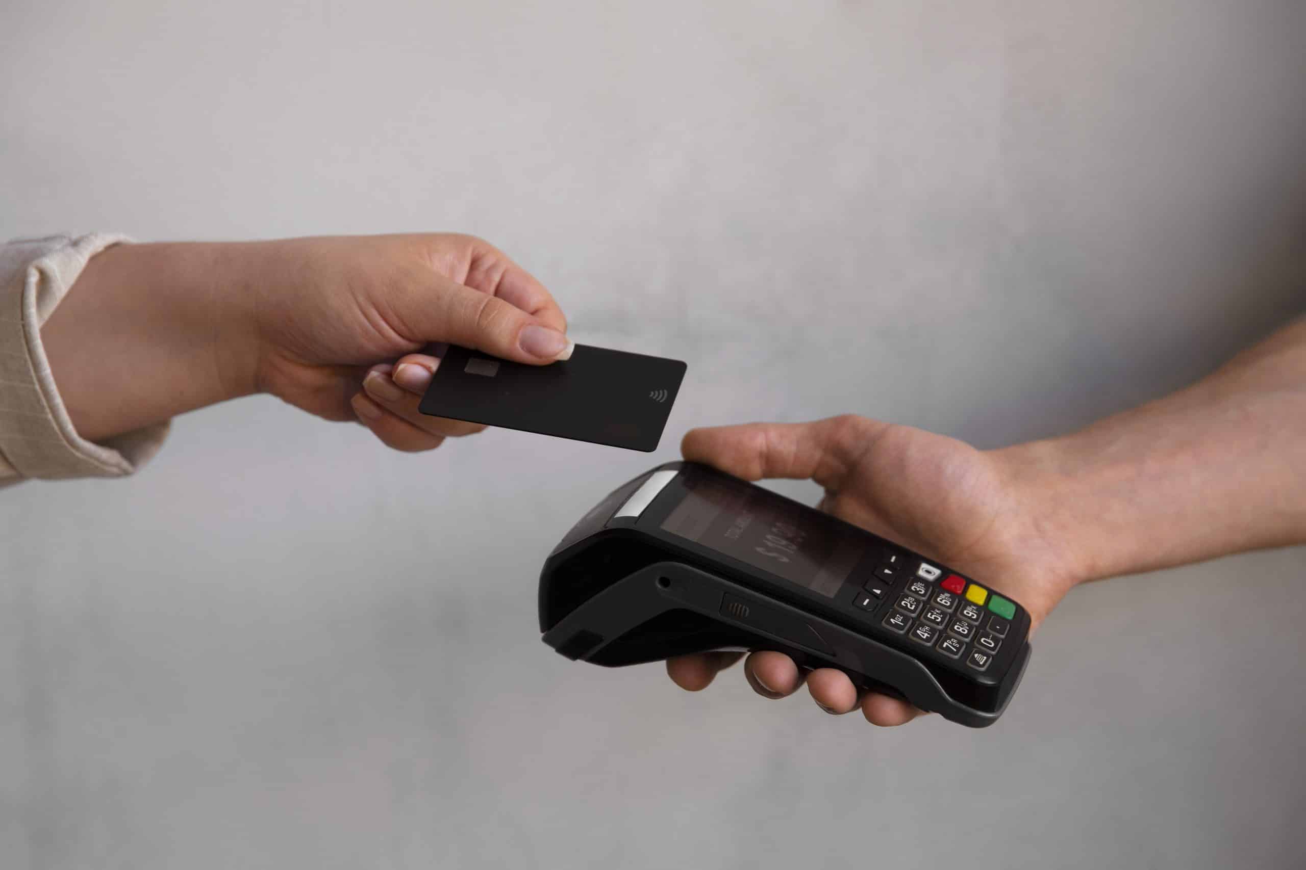 Cliente realizando pagamento por aproximação com cartão preto em uma máquina de cartão moderna, demonstrando a praticidade da tecnologia contactless no comércio atual.