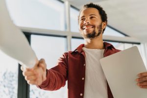 Homem sorridente aperta a mão de outra pessoa enquanto segura um notebook, simbolizando a conclusão bem-sucedida de um processo de empréstimo pessoal, com confiança e satisfação no atendimento recebido.