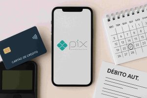 Celular exibindo a tela inicial do sistema Pix ao lado de cartão de crédito, maquininha de pagamento, calendário marcado no dia 21 e formulário de débito automático, representando organização financeira e pagamentos digitais.
