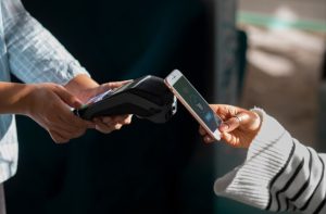 Pessoa utilizando a tecnologia de pagamento por aproximação com smartphone em uma maquininha, representando praticidade nas transações e a importância do controle sobre o limite transacional no dia a dia.