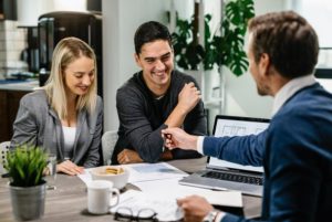 Casal sorridente em reunião com consultor financeiro, recebendo explicações sobre documentos e condições de contrato, simbolizando a negociação de um empréstimo com garantia para alcançar objetivos pessoais.