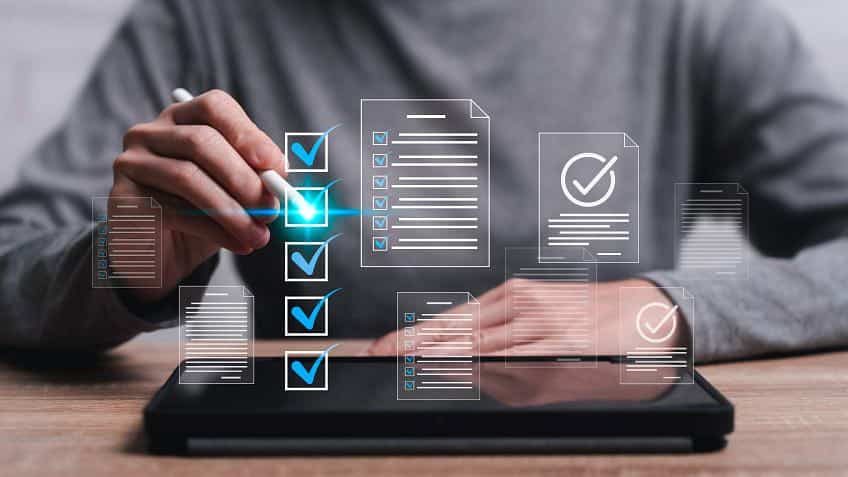 Pessoa utilizando uma caneta digital em um tablet com ícones de listas de verificação flutuantes, representando a análise e aprovação de um empréstimo pessoal de forma rápida e digital.